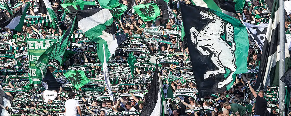 Fußballfans des SC Preußen Münster jubeln und schwenken Schals und Flaggen im LVM Preußenstadion